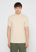 Mann trägt ein beiges kurzärmeliges Poloshirt und olivgrüne Hose, steht vor einem einfarbigen hellgrauen Hintergrund.