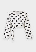 Weiße Langarm-Wickelbluse mit großen schwarzen Polka-Dots und einem vorn gebundenen Gürtel, dargestellt auf einfachem weißem Hintergrund.
