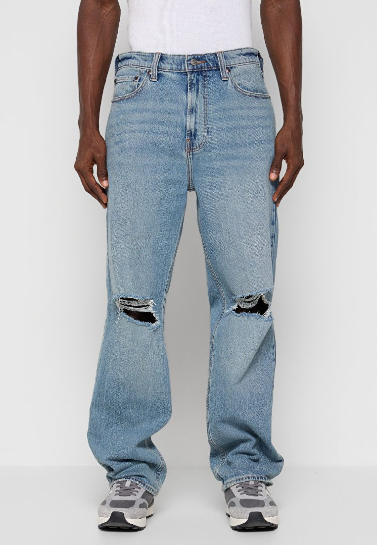Hellblaue Denim-Jeans mit lockerem Schnitt, großen Rissen an den Knien, fünf Taschen und traditionellem Knopfverschluss.