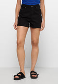 Schwarze Denim-Shorts mit klassischer Passform, fünf Taschen und Knopfverschluss. Getragen mit schwarzen Riemchensandalen vor einem neutralen Hintergrund.