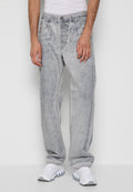 Mann in hellgrauen Acid-Wash-Jeans und weißen Sneakern, der vor einem einfarbigen grauen Hintergrund steht.