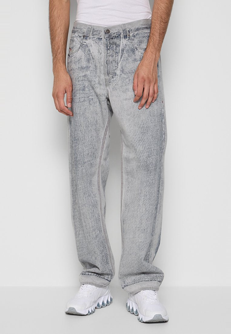 Mann in hellgrauen Acid-Wash-Jeans und weißen Sneakern, der vor einem einfarbigen grauen Hintergrund steht.