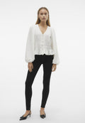 Weiße Peplum-Bluse aus strukturiertem Stoff, mit V-Ausschnitt und Knopfverschluss; kombiniert mit schwarzen, engen Hosen und schwarzen, spitz zulaufenden Schuhen.