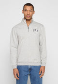 Grauer Pullover mit einem halbhohen Reißverschlusskragen. Verfügt über ein marineblaues "GAP"-Logo auf der Brust und gerippte Bündchen. Wird mit blauen Jeans getragen.