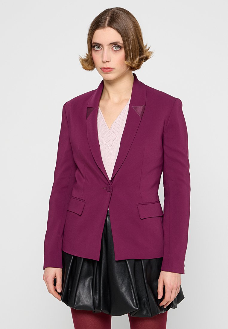 Magenta Blazer mit Reverskragen, einreihigem Knopfverschluss und zwei vorderen Taschen. Über einem hellrosa Pullover und einem schwarzen Lederröcke getragen.