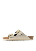 Rutschschuh-Sandale mit zwei verstellbaren goldenen Schnallen, strukturiertem beigen Obermaterial, Korkfußbett und hellbeigem geriffelten Schuhsohle.
