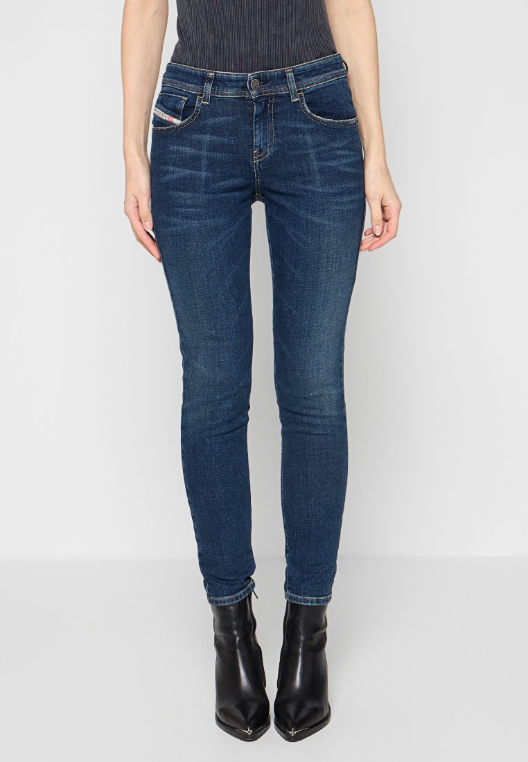 Schmale Jeans aus dunkelblauem Denim mit fünf Taschen, genähten Details und Reißverschluss. Kombiniert mit schwarzen Ankle Boots mit hohen Absätzen.