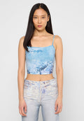 Gekürztes Tanktop aus leicht blauem Stoff mit einem grafischen Druck. Die Träger sind dünn und es hat einen quadratischen Ausschnitt. Texturierte Denim-Jeans runden das Outfit ab.