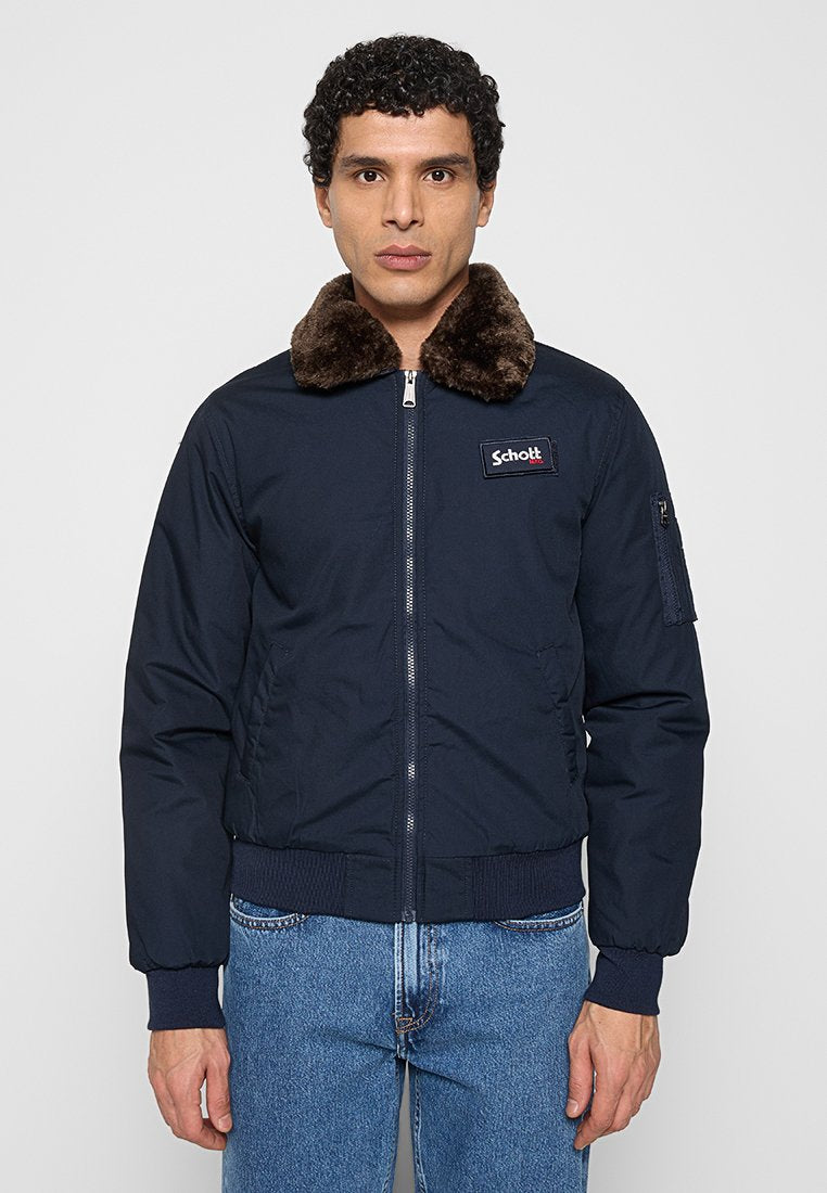 Marineblaue Bomberjacke mit braunem Pelzkragen, Reißverschluss, gerippten Bündchen und Saum sowie seitlichen Taschen. Auf der Brust befindet sich ein Logo-Patch.