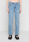 Hellblaue Jeans mit geradem Bein, getragen mit schwarzen Spaltzeh-Schuhen, gezeigt von der Hüfte bis zu den Füßen vor einem hellgrauen Hintergrund.