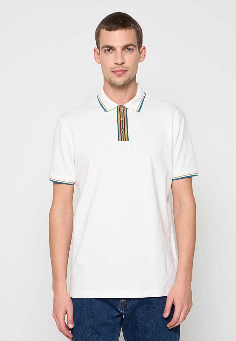 Weißes Poloshirt aus Baumwolle mit einem mehrfarbig gestreiften Kragen und Knöpfen. Kurze Ärmel mit kontrastierenden Akzenten. Kombiniert mit blauen Jeans.
