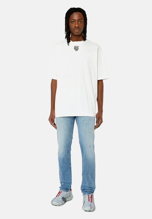 Mann steht, trägt ein weißes, übergroßes T-Shirt mit einem kleinen schwarzen Logo, hellblaue Jeans und graue Sneaker mit roten Schnürsenkeln.