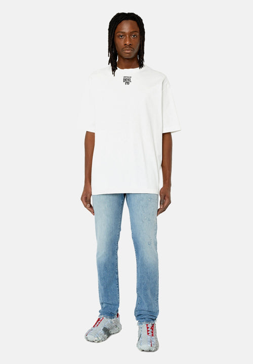 Mann steht, trägt ein weißes, übergroßes T-Shirt mit einem kleinen schwarzen Logo, hellblaue Jeans und graue Sneaker mit roten Schnürsenkeln.