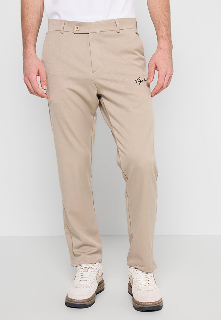 Beige Hose mit geradem Bein, ausgestattet mit einem Knopfverschluss und gesticktem Logo-Detail auf der linken Seite. Kombiniert mit weißen Sneakern.