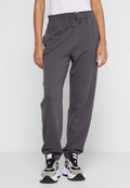 Graue Baumwoll-Jogginghosen mit elastischem Bund, verstellbarem Kordelzug und seitlichen Taschen, kombiniert mit schwarzen und beige dicken Sneakers.
