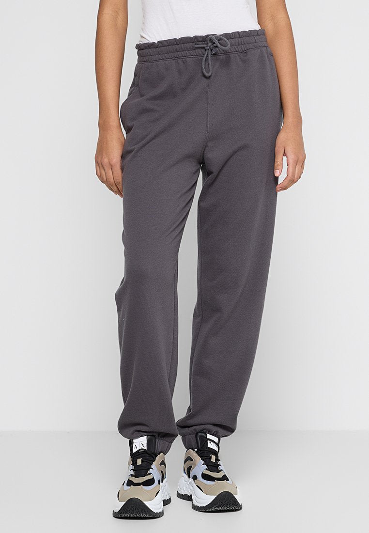 Graue Baumwoll-Jogginghosen mit elastischem Bund, verstellbarem Kordelzug und seitlichen Taschen, kombiniert mit schwarzen und beige dicken Sneakers.