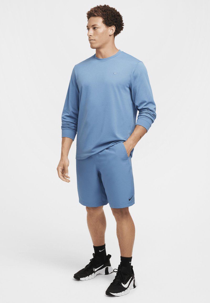 Hellblaues Langarmhemd und passende Shorts mit Nike-Logo. Schwarze Sportschuhe mit strukturiertem Sohlenprofil und Knöchelstütze.