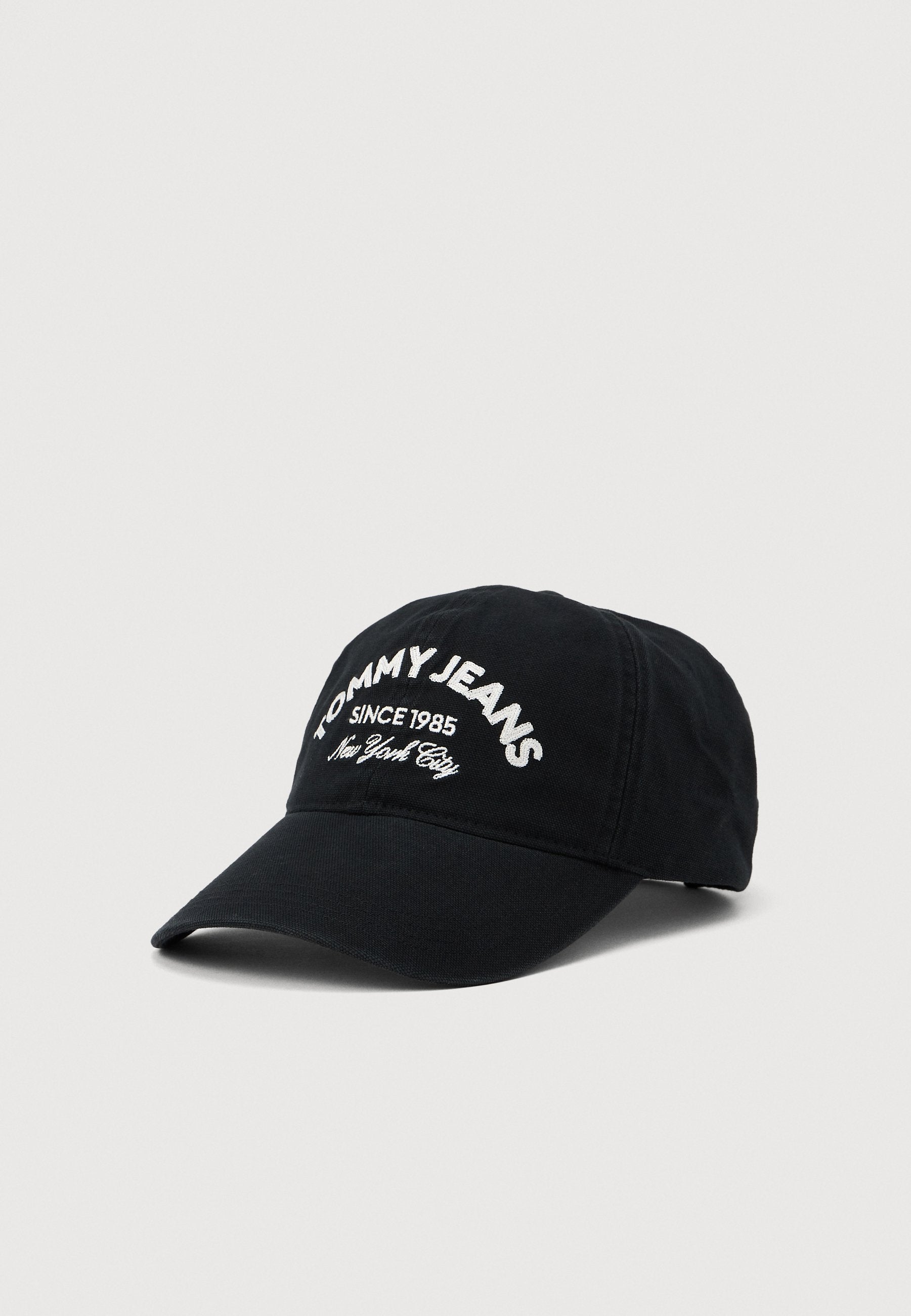 Schwarze Baseballmütze mit gebogenem Schirm, die auf der Vorderseite weiß gestickten Text "TOMMY JEANS SINCE 1985 New York City" zeigt.