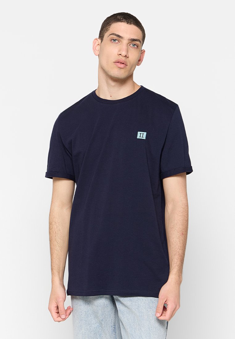 Dunkelblaue Baumwoll-T-Shirt mit kurzen Ärmeln. Verfügt über ein kleines hellblaues Quadrat-Logo mit "II" auf der linken Brust. Einfaches, lässiges Design.
