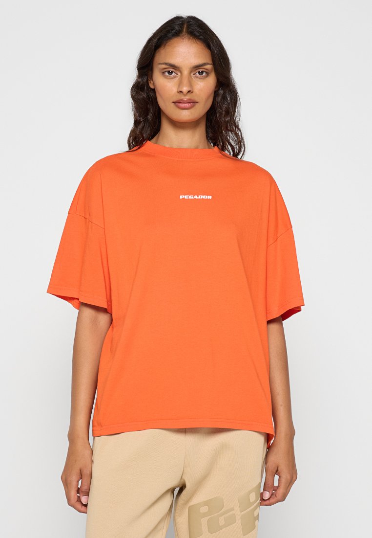 Übergrößenshirt in Orange aus Baumwolle, mit einem gerippten Rundhalsausschnitt und einem weißen "PEGADOR"-Logo auf der Brust. Glatte Textur.