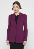 Eine Frau mit heller Haut und kurzen braunen Haaren trägt einen lila maßgeschneiderten Blazer über einem schwarzen Top und steht vor einem schlichten weißen Hintergrund.