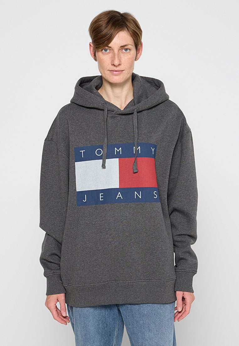 Grauer Kapuzenpullover mit einem großen rechteckigen Grafikdesign in Marineblau, Rot und Grau. Mit Kordelzügen und lockerem Schnitt. Markenlogo gut sichtbar.