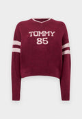 Bordeauxroter kurzer Pullover mit V-Ausschnitt, versehen mit weißer "TOMMY 85" Beschriftung und gestreiften weißen Akzenten an den Ärmeln. Weiche Strickstruktur.