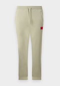Hellbeige Jogginghose mit elastischem Bund, Kordelzug, Seitentaschen, gerippten Bündchen und einem kleinen roten "HUGO"-Logo-Patch am rechten Oberschenkel.