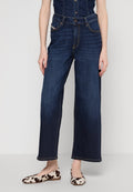 Dunkelblaue, weite Jeans mit hoher Taille, ausgestattet mit vorderen Taschen und einem Knopfverschluss; getragen mit cremefarbenen Ballerinas mit Kuhflecken.