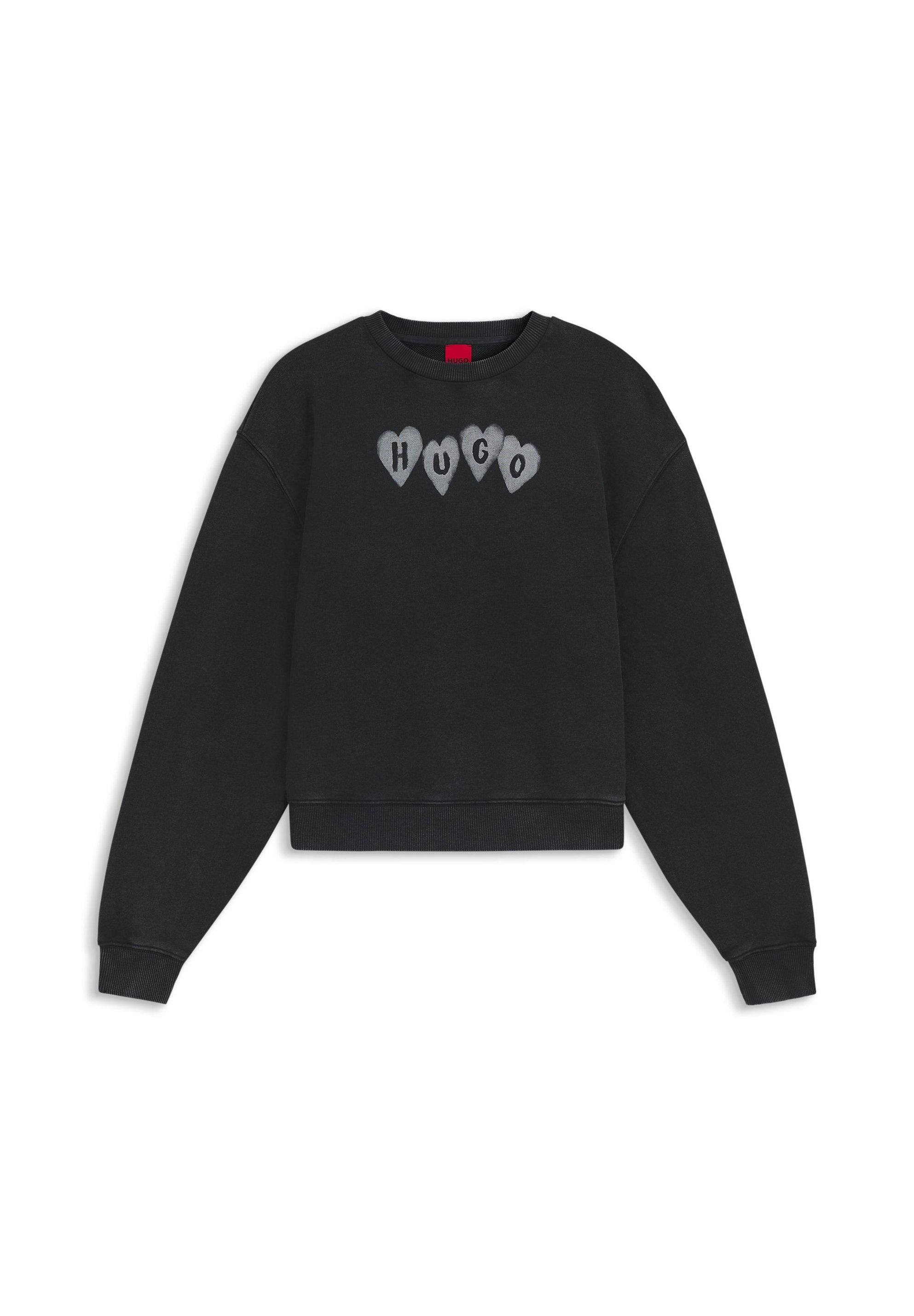 Schwarzer Baumwollpullover mit Rundhalsausschnitt, gerippten Bündchen und Saum. Mit grauer herzförmiger Schrift, die "HUGO" über der Brust buchstabiert.