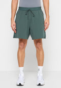 Grüne Shorts mit glatter Textur, elastischem Taillenbund, verstellbarem Kordelzug und Seitentaschen, getragen mit weißen Sportschuhen und Socken.