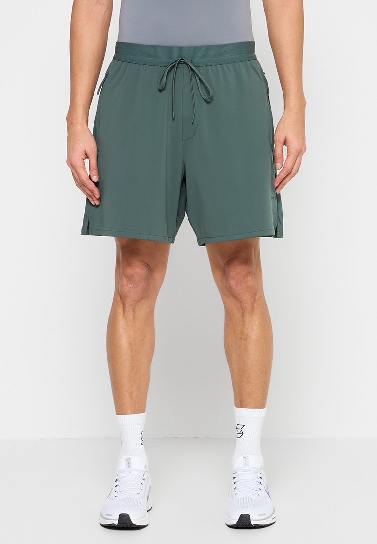 Grüne Shorts mit glatter Textur, elastischem Taillenbund, verstellbarem Kordelzug und Seitentaschen, getragen mit weißen Sportschuhen und Socken.