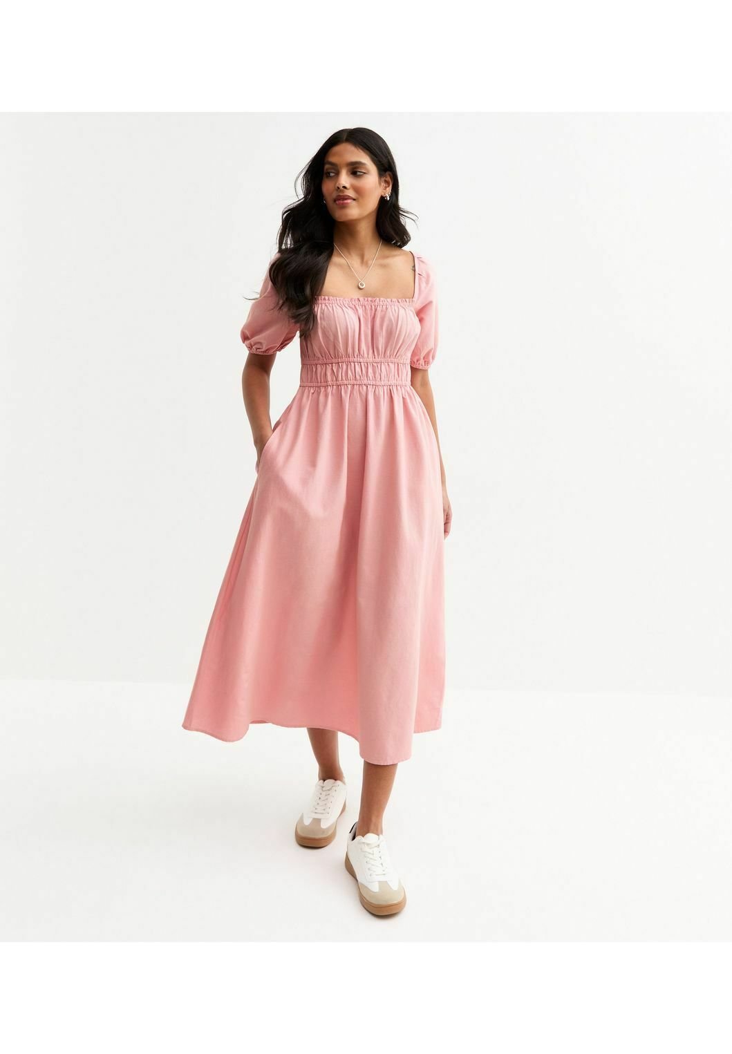 Rosa Midikleid mit Puffärmeln, quadratischem Ausschnitt, geraffter Taille, seitlichen Taschen und glatter Textur, kombiniert mit weißen Sneakern.