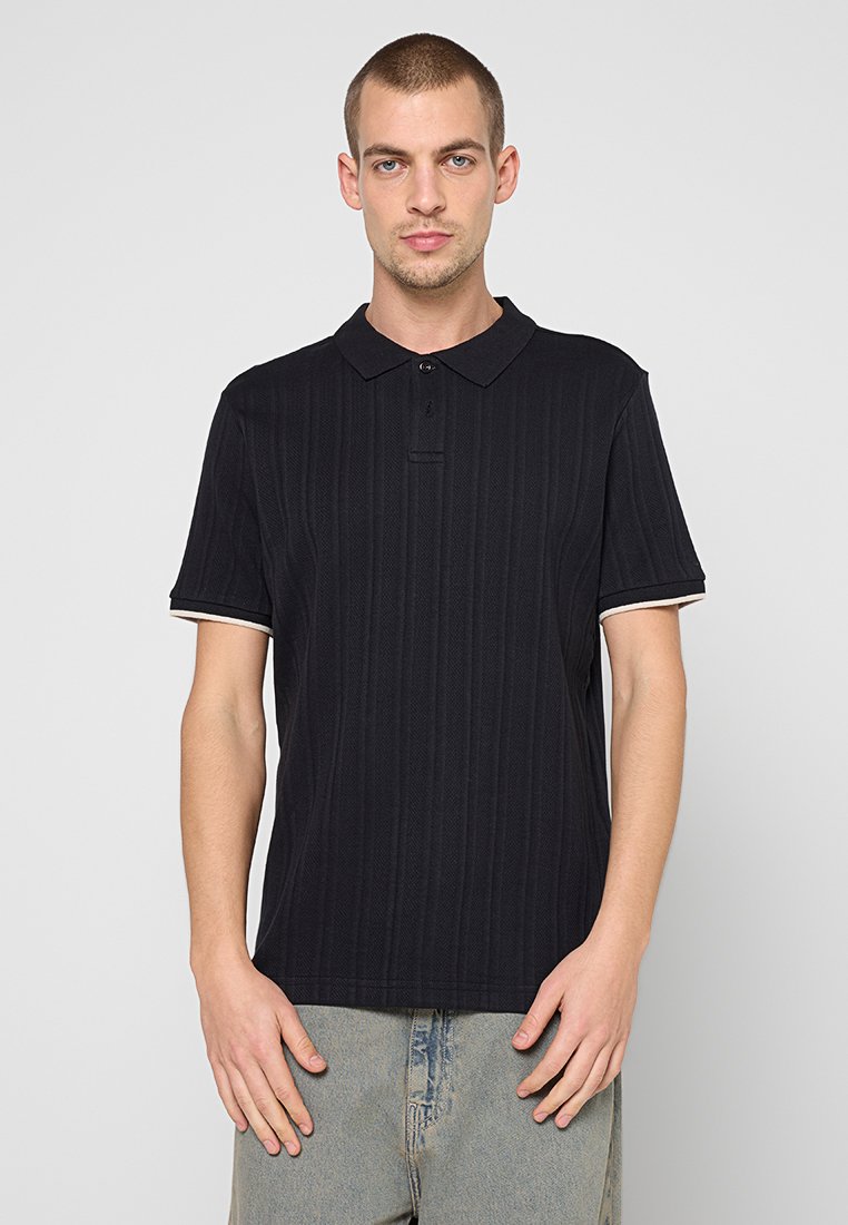 Schwarzes Poloshirt mit vertikaler Rippenstruktur, kurzen Ärmeln und kontrastierenden weißen Akzenten am Kragen und an den Ärmeln. Slim-Fit-Design.