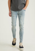 Hellblaue Slim-Fit-Jeans mit Verwaschungen und Used-Look-Details, kombiniert mit marineblauen Sneakers mit beigen Schnürsenkeln und einer strukturierten Oberfläche.