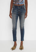 Ausgeblichene blaue Denim-Jeans mit schmaler Passform, die über Distressed-Details und ein traditionelles Five-Pocket-Design verfügen. Getragen mit grünen, gemusterten Slippern.