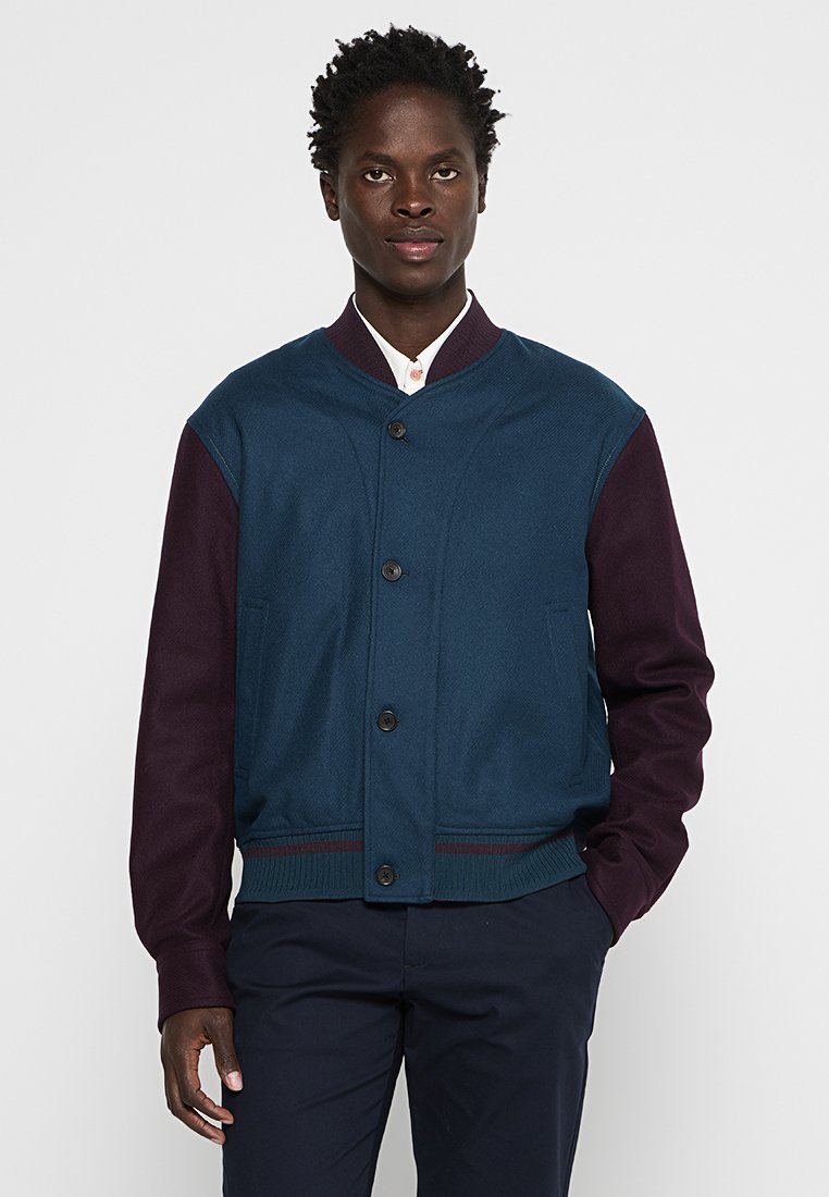 Herren Bomberjacke mit dunkelblauem Oberteil, bordeauxfarbigen Ärmeln, Knopfverschluss, geripptem Kragen und kontrastierender Textur. Mit Fronttaschen.