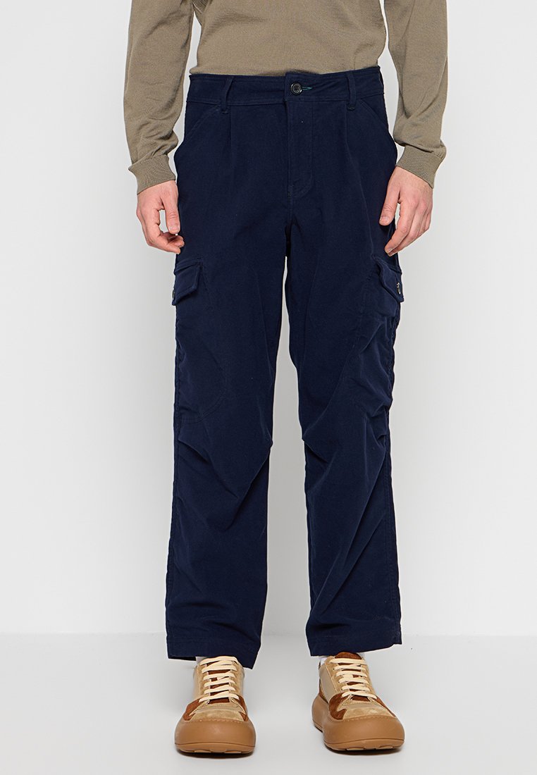 Marineblaue Cargo-Hosen aus strapazierfähigem Stoff, ausgestattet mit Seitentaschen, geradem Schnitt und Knopfverschluss in der Taille. Schuhe im Vordergrund.