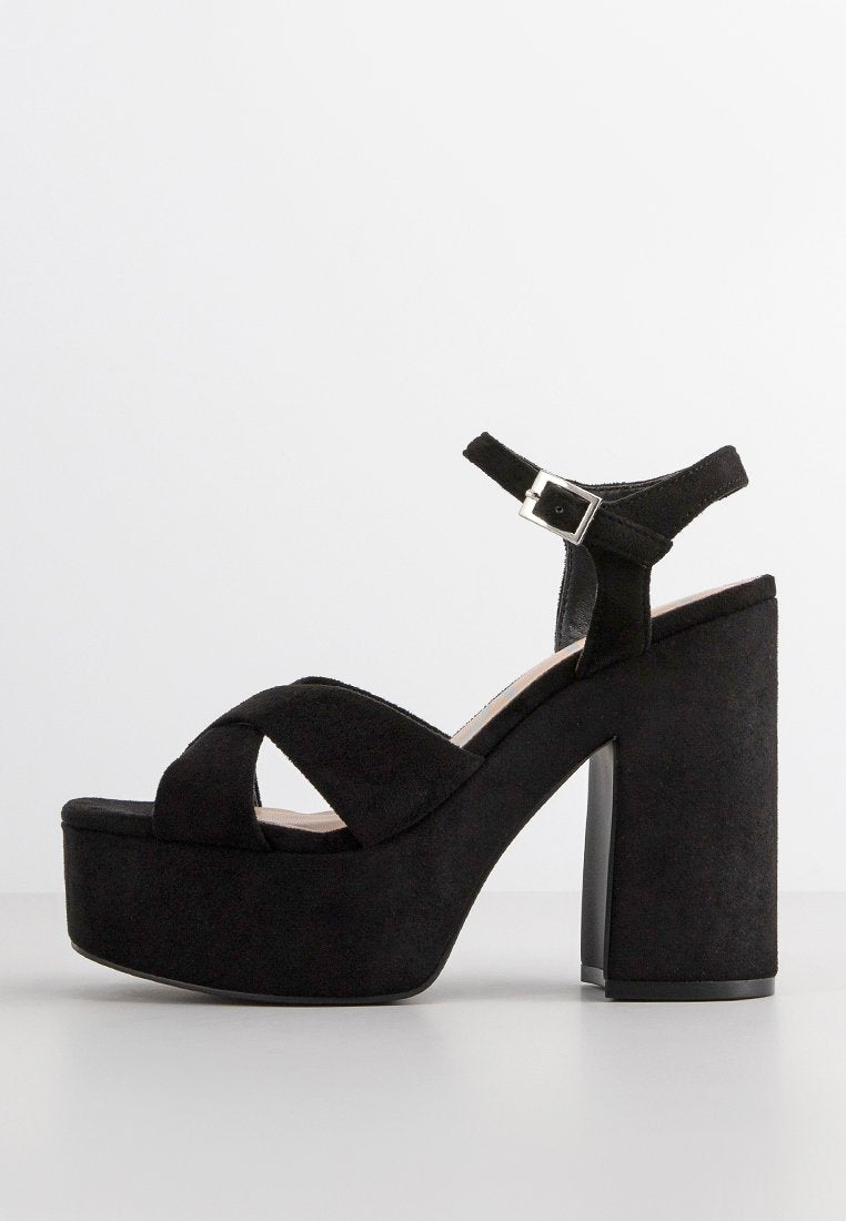 Schwarze Wildleder-Plateausandalen mit einem breiten Riemen über den Zehen, einem Knöchelriemen mit einer silbernen Schnalle und einem klobigen hohen Absatz.