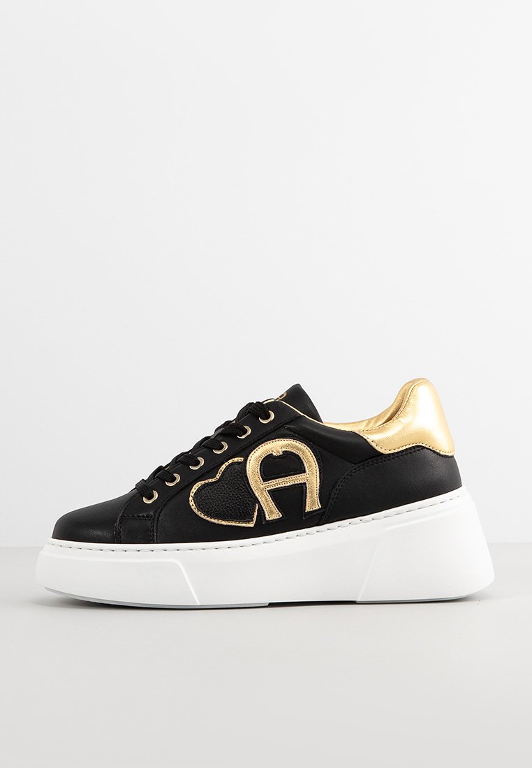 Schwarze Ledersneaker mit goldenen Akzenten, ausgestattet mit einem auffälligen Herz- und Buchstaben-A-Design, dicke weiße Sohle und runder Zehenpartie.