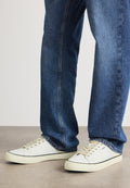 Weiße Canvas-Sneaker mit beigen Schnürsenkeln und schwarzen Akzenten, kombiniert mit blauen Jeans im geraden Schnitt und heller Waschung.