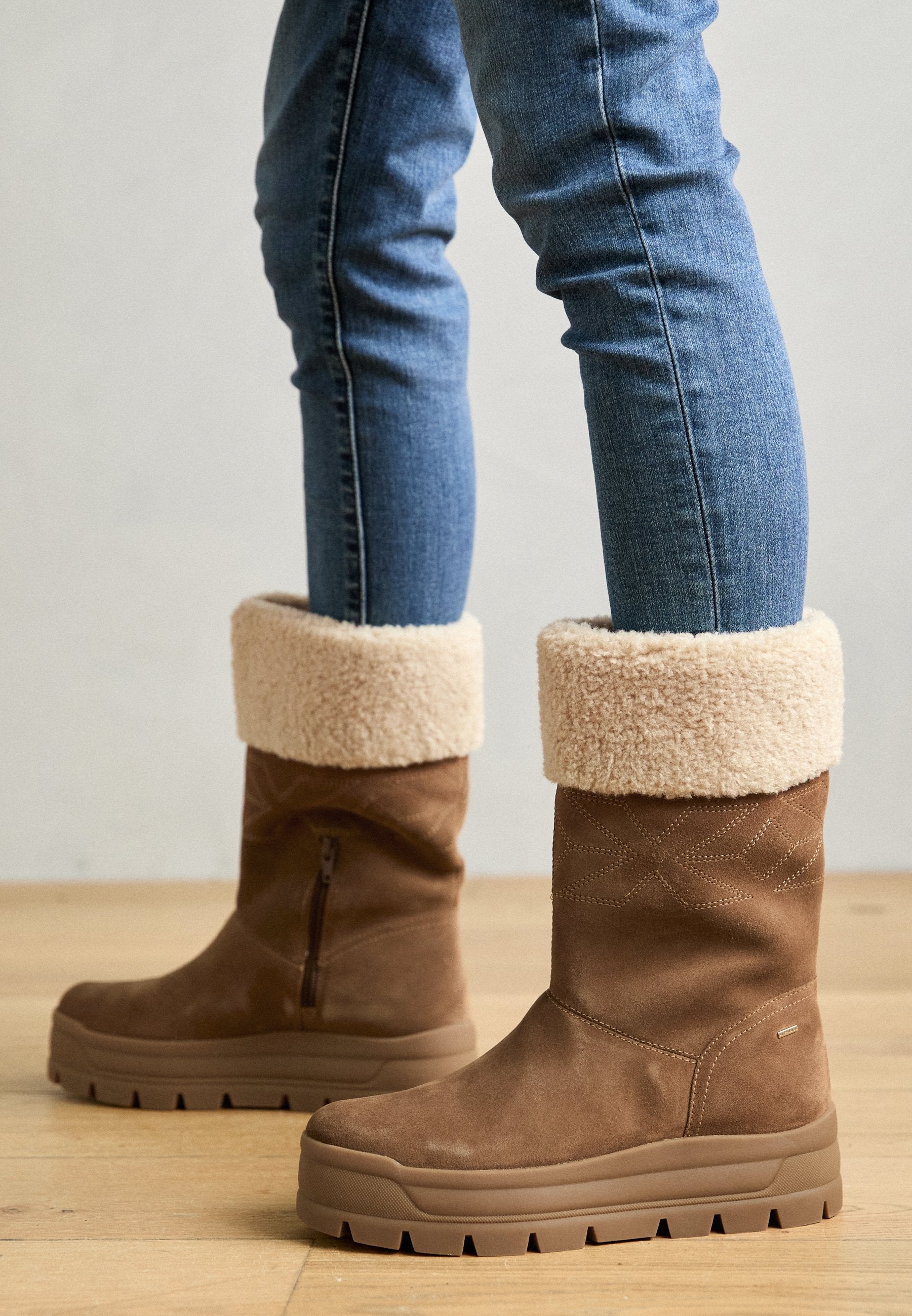 Braune Wildleder-Ankle Boots mit einem cremefarbenen Kunstfellkragen, seitlichem Reißverschluss und dicker Gummisohle mit robustem Profil.