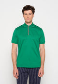 Mann steht vor schlichtem Hintergrund, trägt ein leuchtend grünes Poloshirt mit gestreiftem Besatz und marineblaue Nadelstreifenhose, schaut nach vorn.