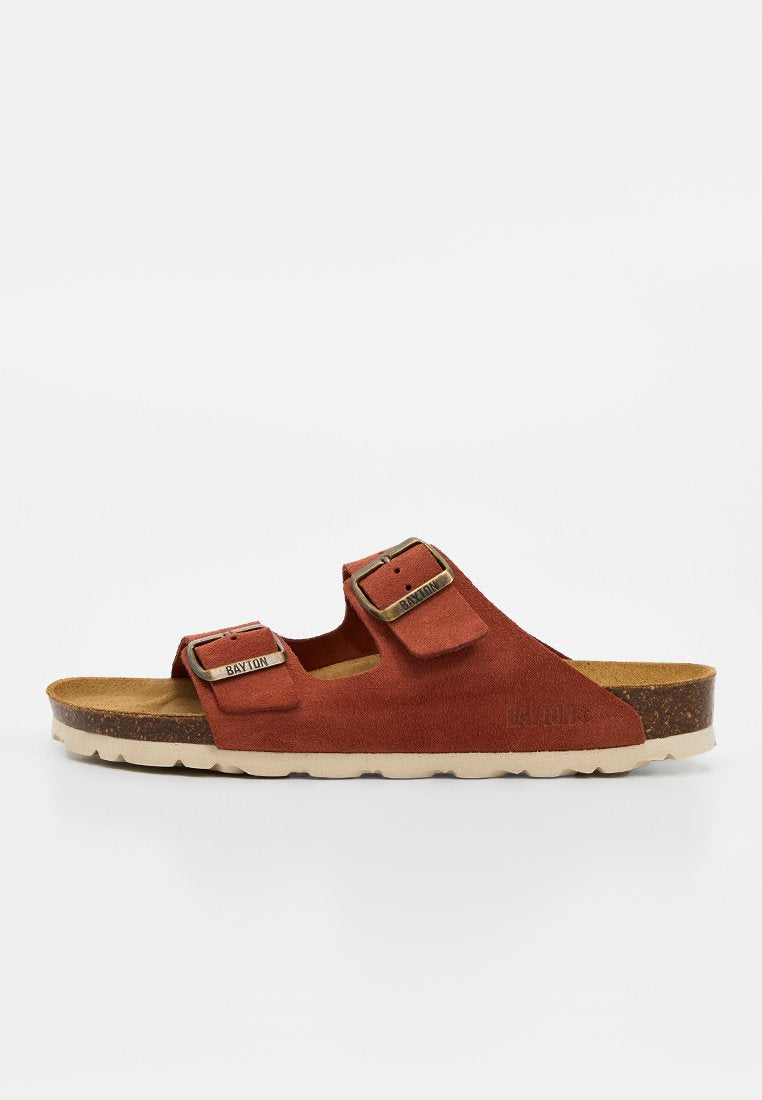 Brauner Wildleder-Slidesandalette mit zwei verstellbaren Metallschnallen und einem Korkfußbett auf weißem Hintergrund.