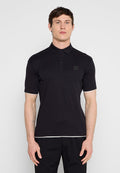 Mann steht und trägt ein schlichtes schwarzes Kurzarm-Poloshirt und schwarze Hose vor einem einfarbigen hellgrauen Hintergrund.