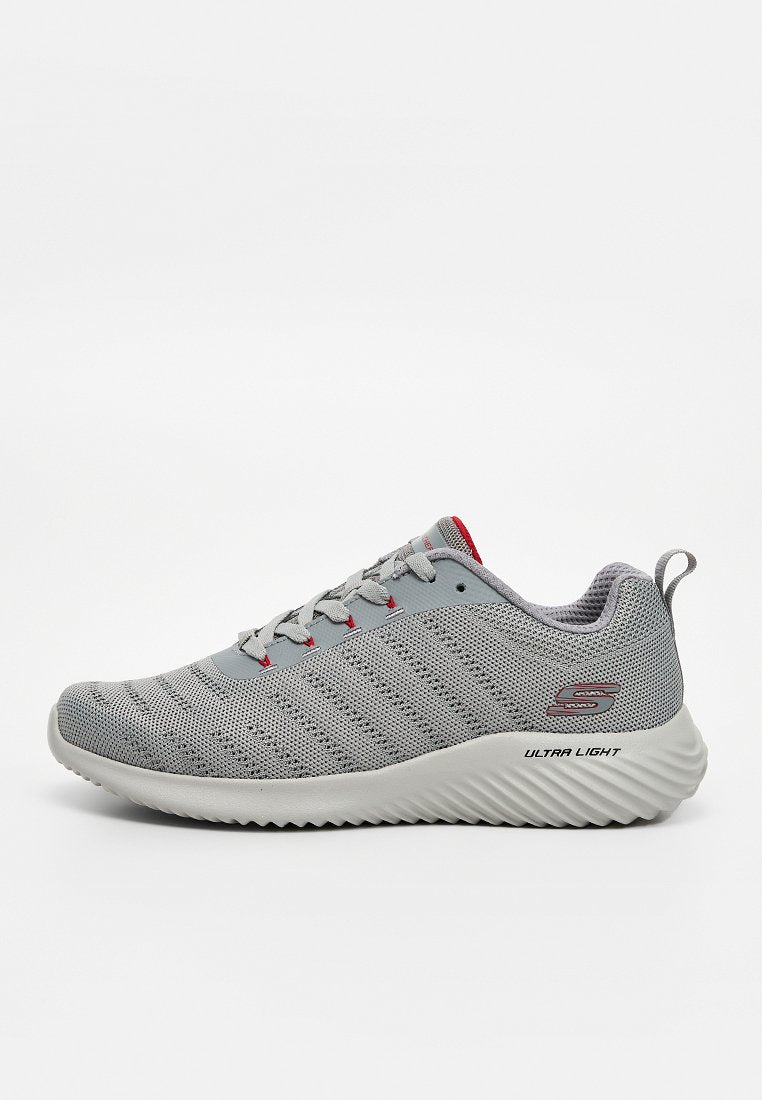 Leichter grauer Sportschuh mit Mesh-Obermaterial, weißer gerippter Sohle, Schnürverschluss, roten Akzenten und Zuglasche hinten.