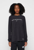 Frau mit lockigem Haar, die ein schwarzes langärmeliges Nike Basketball-Shirt und schwarze Hose trägt, vor einem einfarbigen Hintergrund stehend.