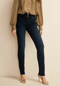 Frau trägt dunkelblaue Skinny Jeans, eine hellbraune Bluse mit langen Ärmeln und gerafften Manschetten sowie silberne High-Heels.