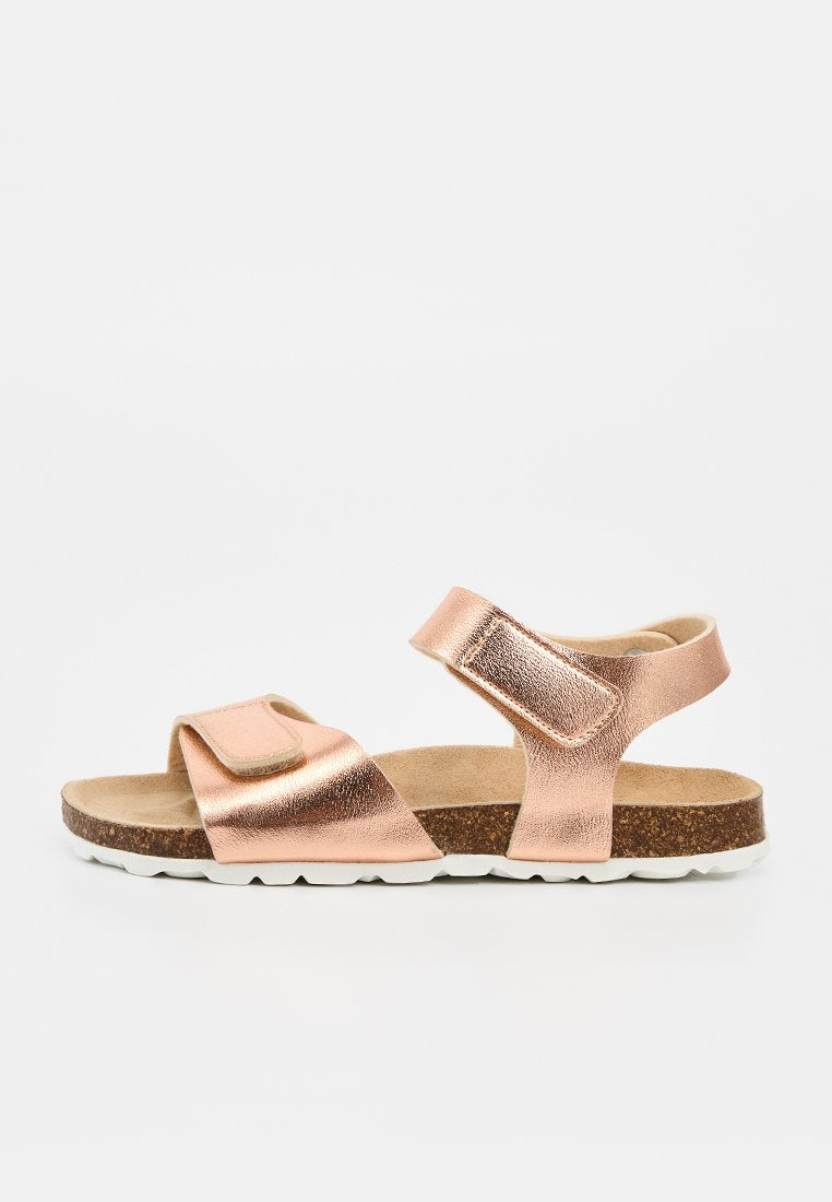 Kindersandale in roségold mit Metallic-Finish, zwei verstellbaren Klettverschlüssen, Korkfußbett und weißer Gummisohle vor einfarbigem Hintergrund.