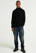 Schwarzer Rollkragenpullover aus weichem Material, kombiniert mit blauen Jeans aus Denim mit einem ausgewaschenen Muster. Das Modell trägt schwarze Wanderschuhe.
